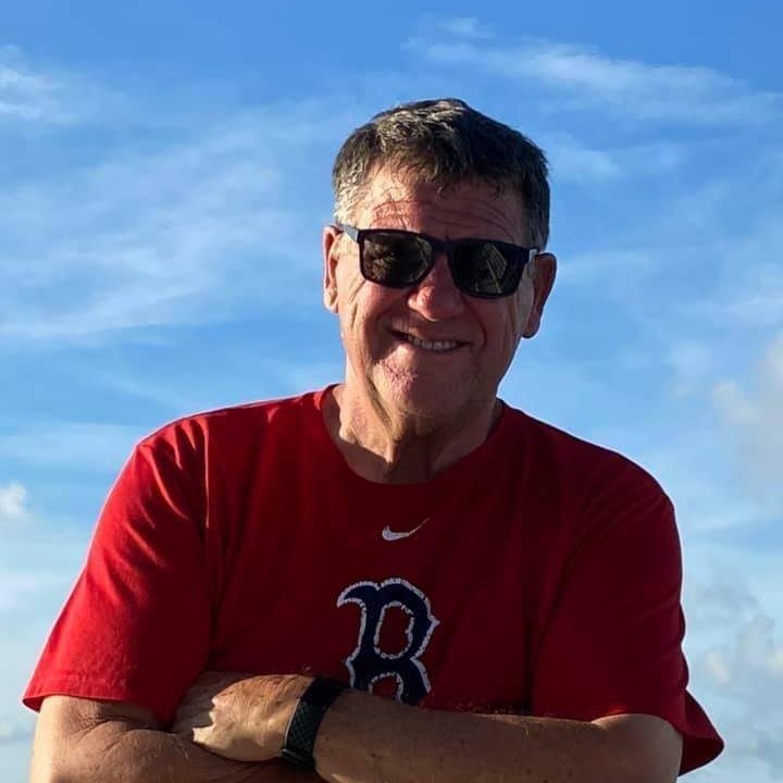 Hombre sonriente con gafas de sol y camiseta roja en un día soleado.