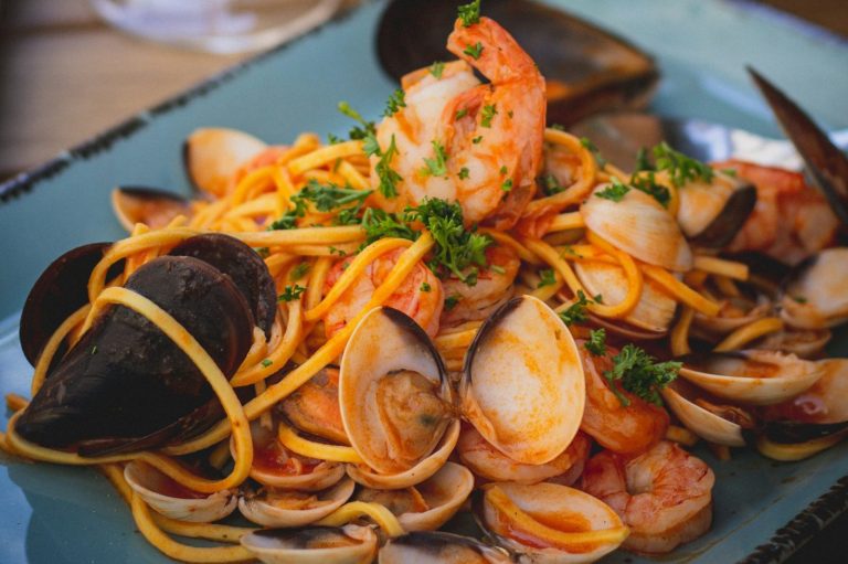 Plato de pasta con mariscos, camarones y perejil fresco, servido en un plato azul.