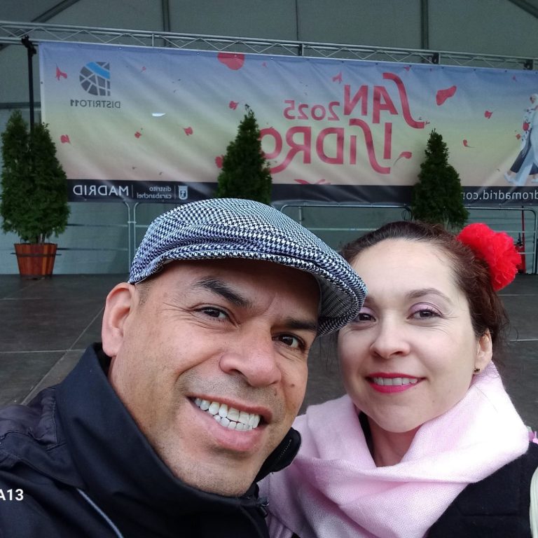 Pareja posando frente a un fondo de flores rosas y un camino iluminado.